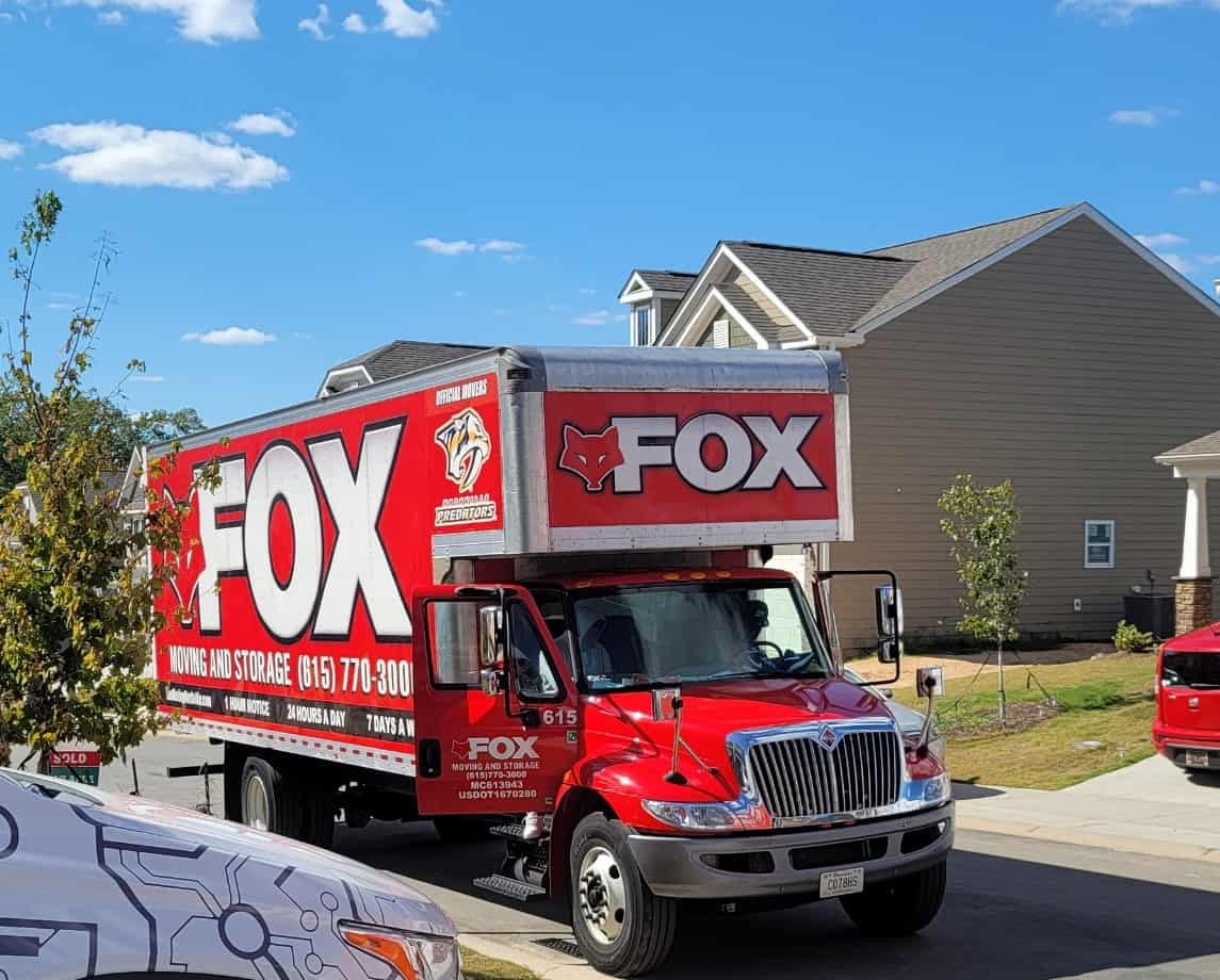 a moving truck of fox moving and storage, branded in red branding, is standing in front of a residential property.