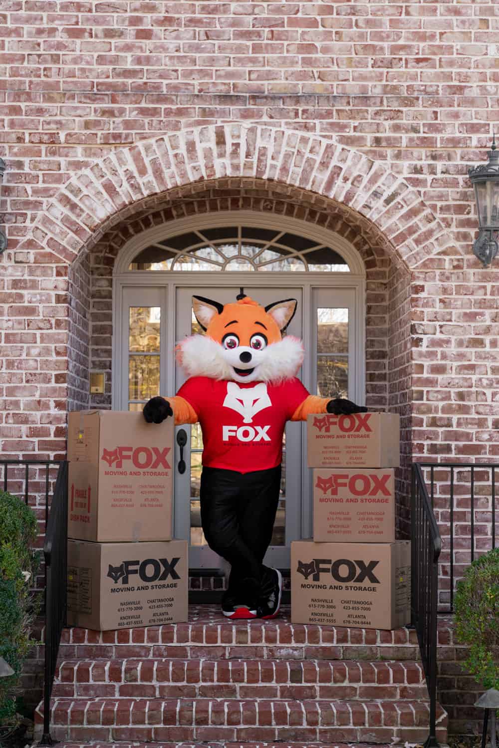 a mascot of fox moving and storage standing in front of a residential house