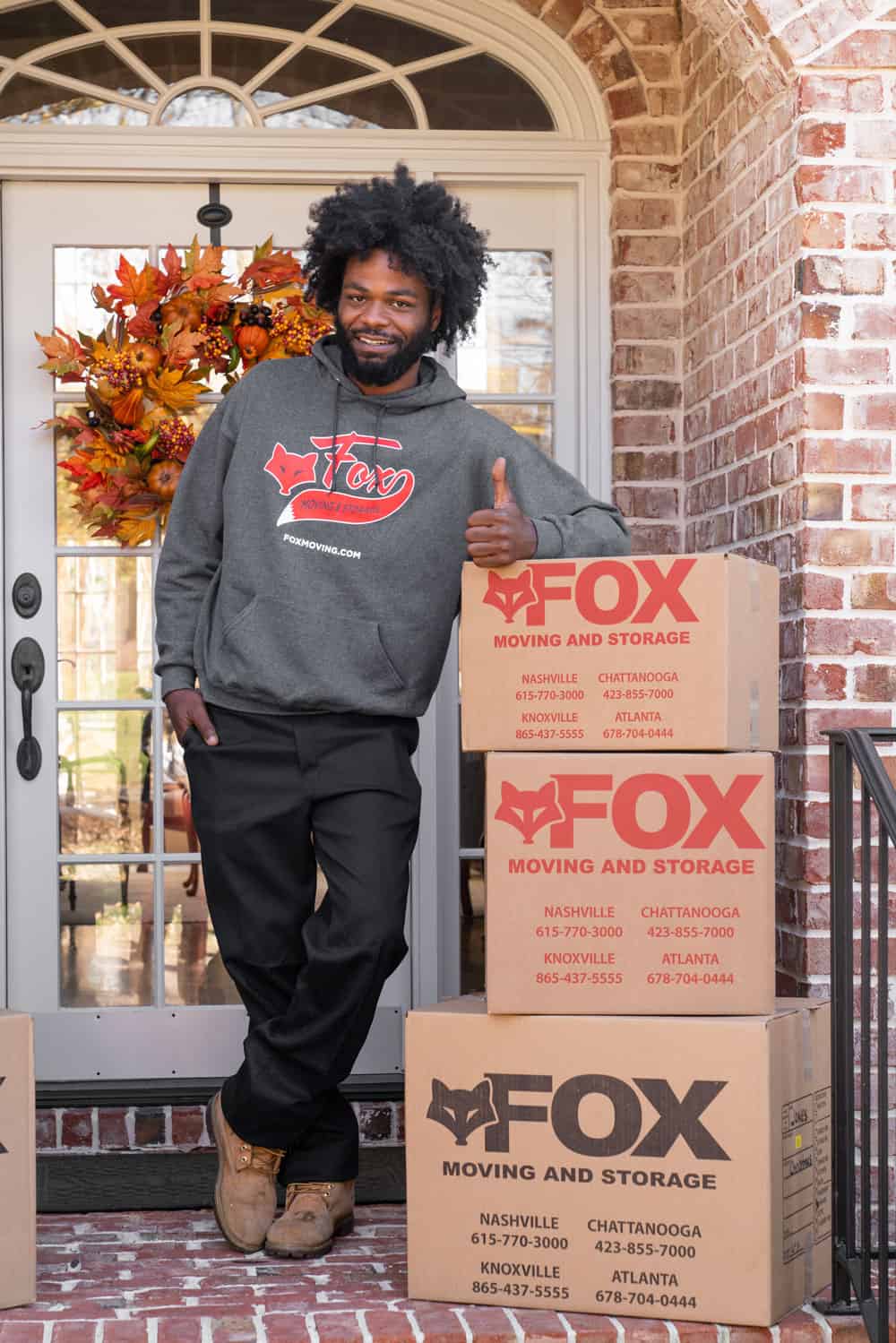 a young man, wearing branded fox moving and storage's hoodie is standing in front of the house smiling