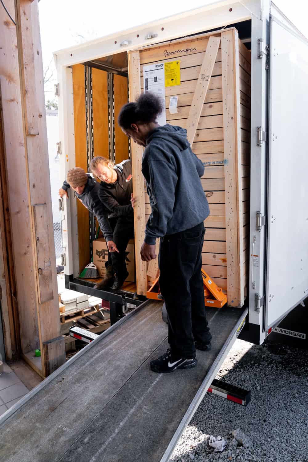 several movers of fox moving and storage are carefully moving large crate out of a moving truck