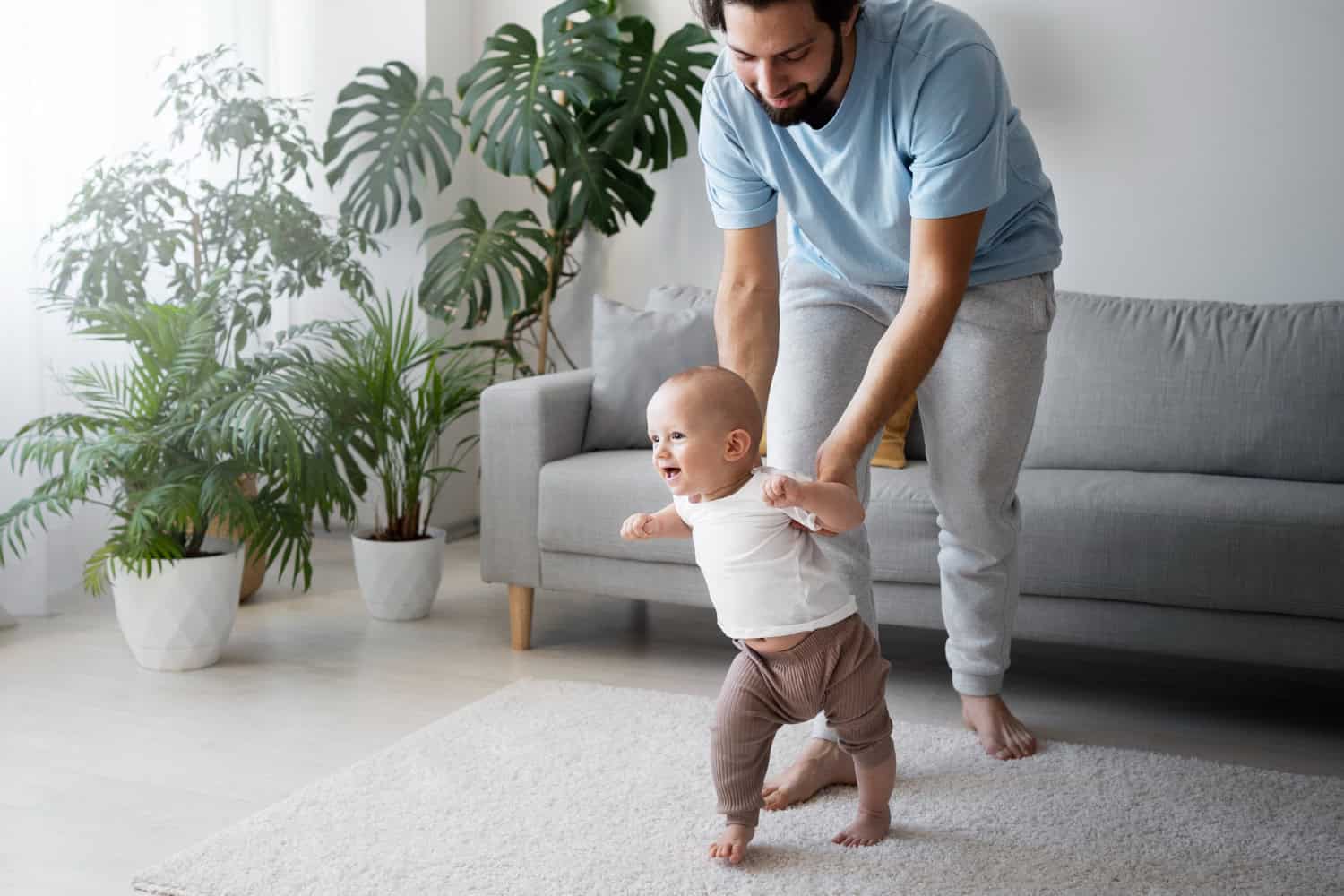 Man helping baby walk in cozy living room.