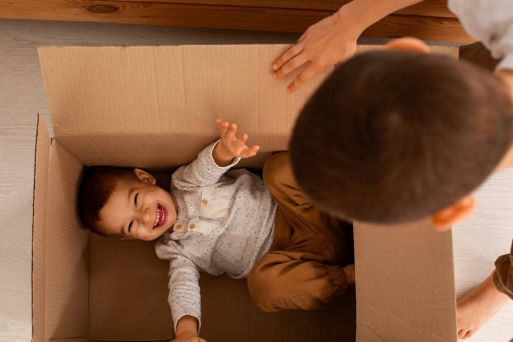 Child laughing inside cardboard box, playful fun scene.